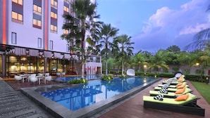 A hotel pool area with lounge chairs, a dining area, and a building with multiple floors. - Harper Purwakarta by ASTON (Bungursari)