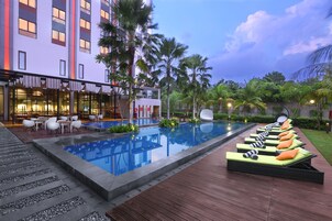 A hotel pool area with lounge chairs, a dining area, and a building with multiple floors.