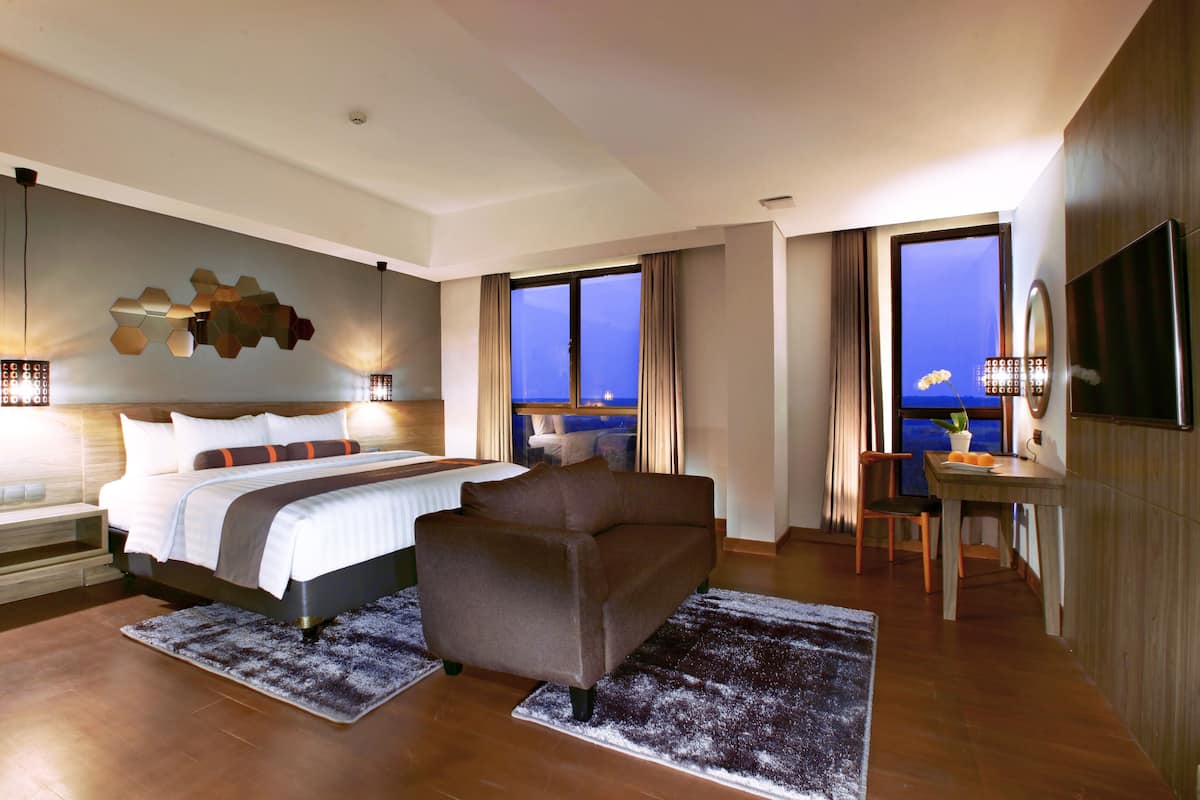 Een moderne hotelkamer met een groot bed, een bank, een zithoek en uitzicht op zee.