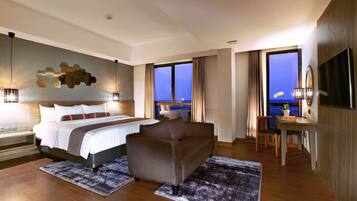 A modern hotel room with a large bed, a sofa, a dining area, and a view of the sea.