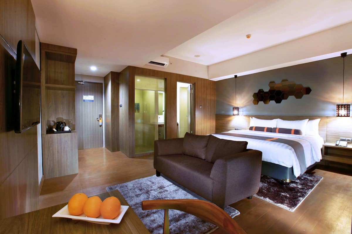 Een moderne hotelkamer met een bank, een eettafel met sinaasappels, een bed met hoofdeinde en een televisie aan de linker muur.