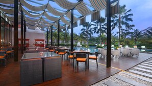 A spacious outdoor lounge area with multiple seating arrangements, a pool, and a view of palm trees. - Harper Purwakarta by ASTON (Bungursari)