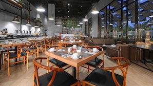 A restaurant with wooden tables and chairs, a bar area, and large windows offering a view of the outside. - Harper Purwakarta by ASTON (Bungursari)
