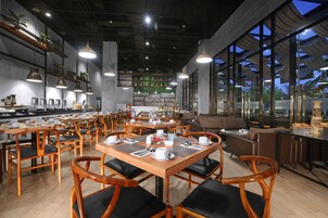 A restaurant with wooden tables and chairs, a bar area, and large windows offering a view of the outside.