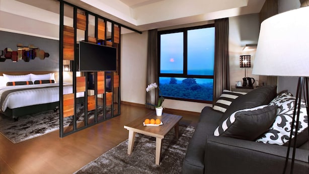 A modern hotel room with a bed, a sofa, a coffee table, and a large window offering a view of the ocean. - Harper Purwakarta by ASTON (Bungursari)