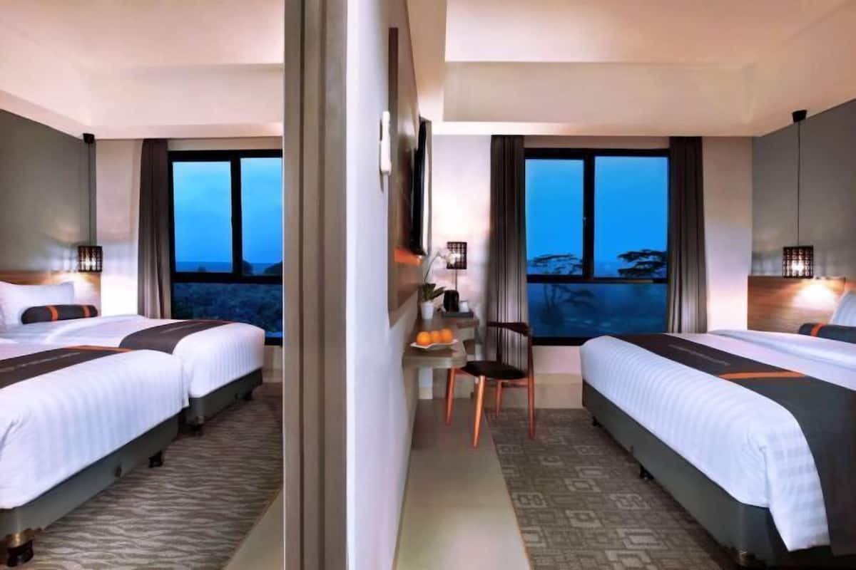 Een hotelkamer met twee bedden, een bureau, een stoel en uitzicht op de omgeving.