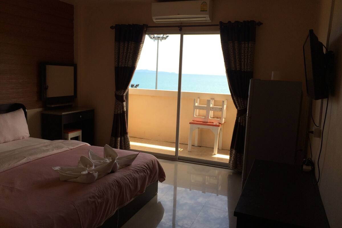 Habitación de hotel con cama, escritorio, silla y vista al mar a través de una puerta corrediza.