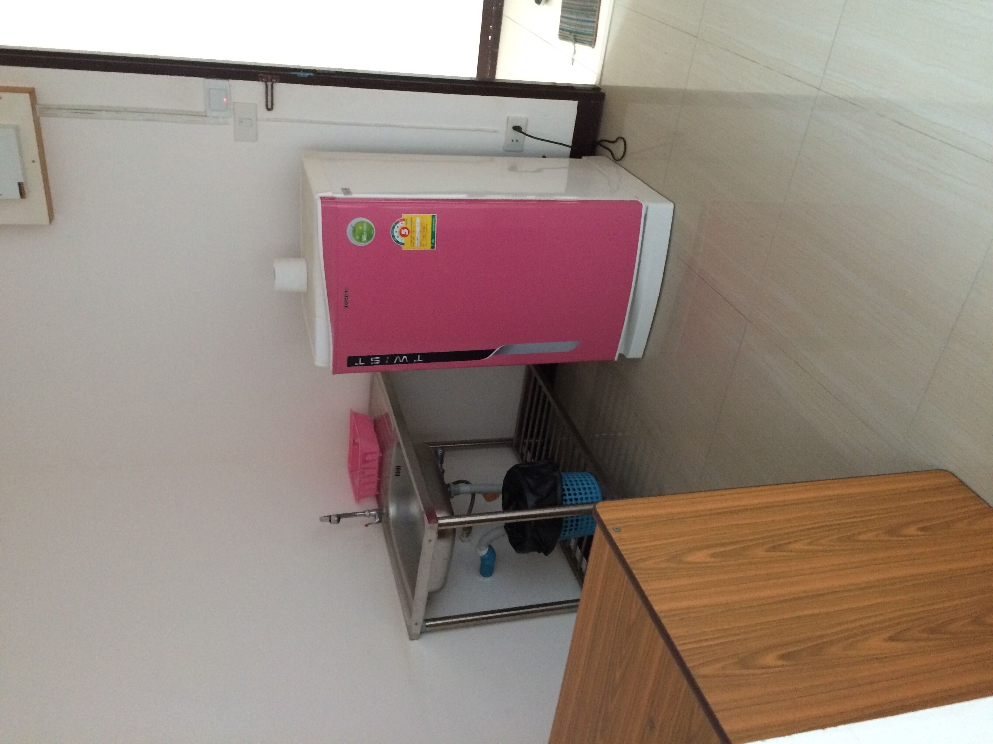 A compact room with a pink air conditioner, a wooden cabinet, and a small shelf with personal items.