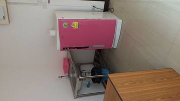 A compact room with a pink air conditioner, a wooden cabinet, and a small shelf with personal items.