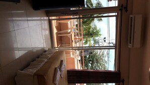 A hotel room with a sofa, a window with a view of palm trees, and an air conditioning unit.