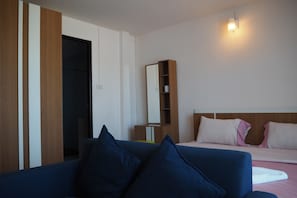Una stanza con un divano blu, un letto con cuscini rosa, un armadio in legno e un comodino.