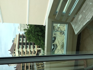 Vista da janela sobre um estacionamento, com uma árvore e edifícios ao fundo.