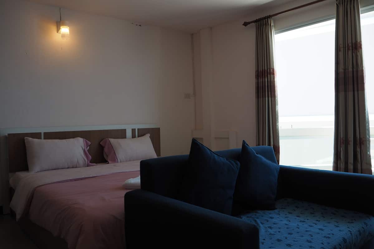 Una habitación de hotel con cama, sofá, ventana con cortinas y una lámpara fijada a la pared.