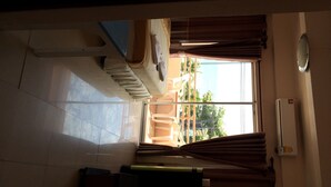 A room with a large window, a ceiling fan, a flat-screen TV, and a desk with a chair.