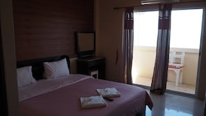 A hotel room with a large bed, a bedside table, a TV, and a balcony with a chair.