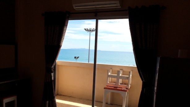 A room with a bed, a chair, and a balcony with a view of the sea.
