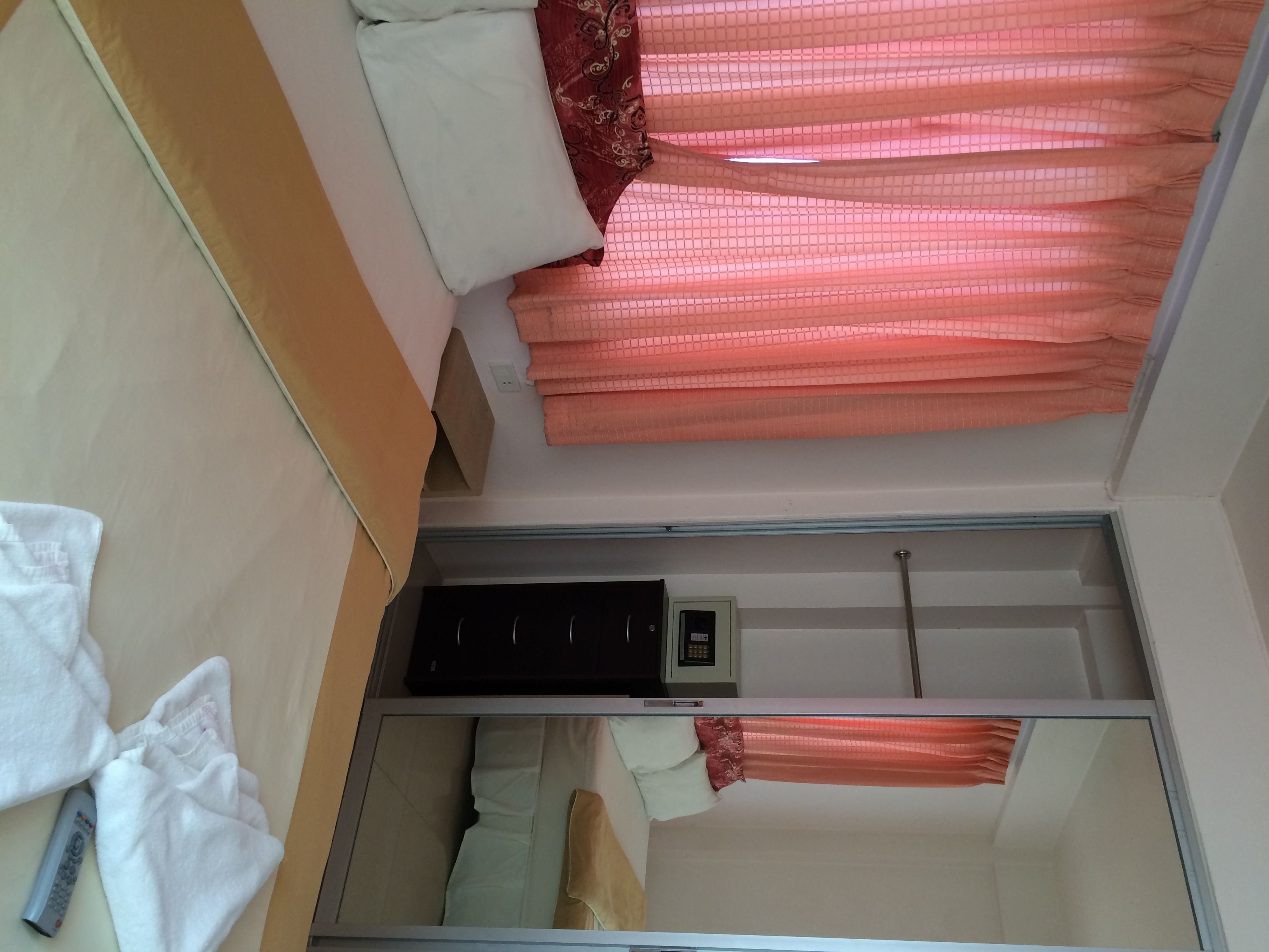 Quarto de hotel com uma cama, um pequeno aquecedor preto e um espelho.