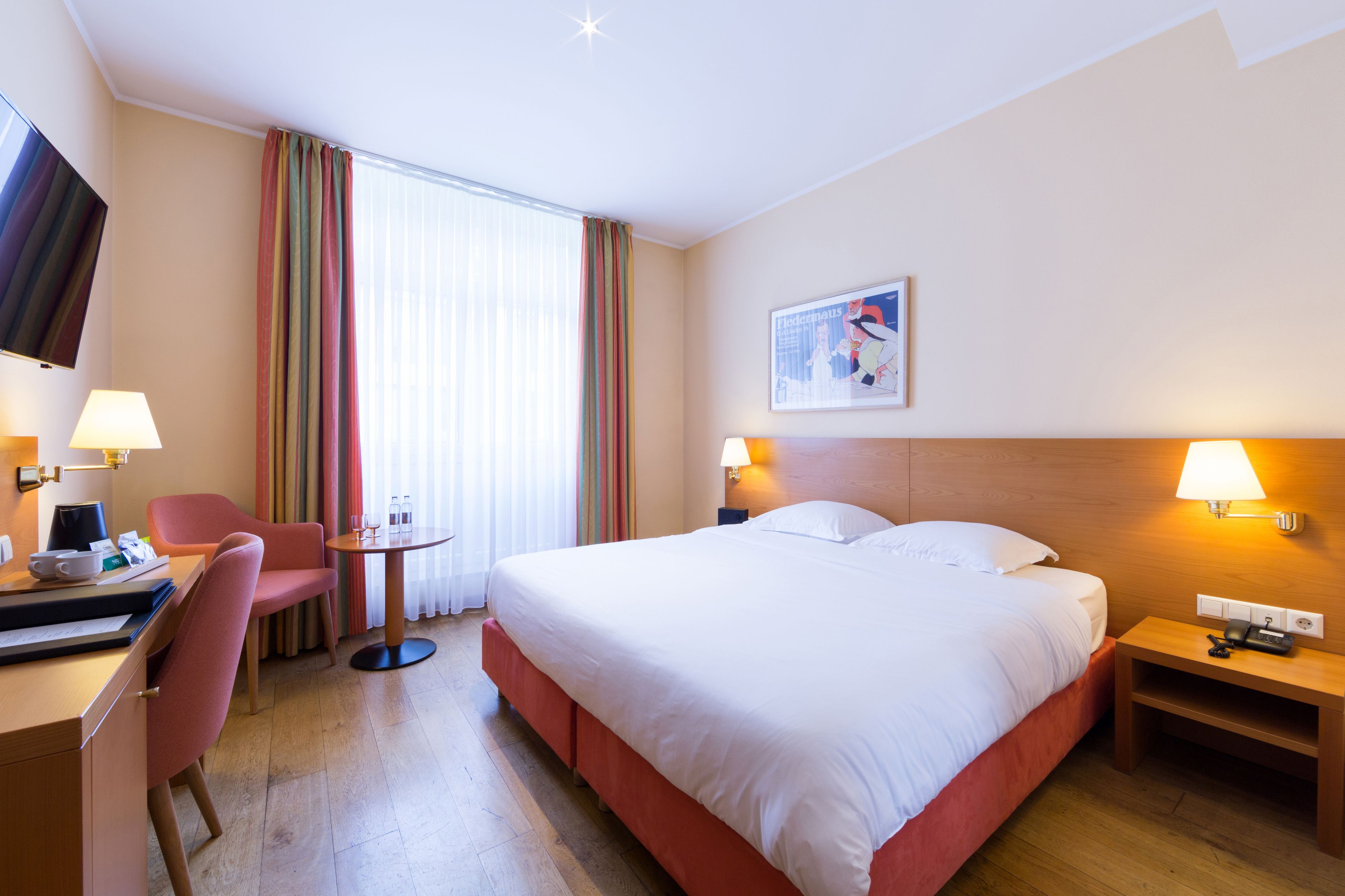 A hotel room with a bed, bedside table, lamp, desk, chair, and a TV.