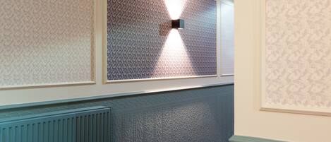 A hallway with patterned wallpaper, a radiator, and a light fixture.