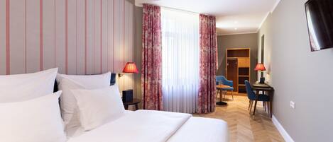 Habitación de hotel con una cama grande, dos lámparas de noche, un escritorio con una silla y un televisor montado en la pared.