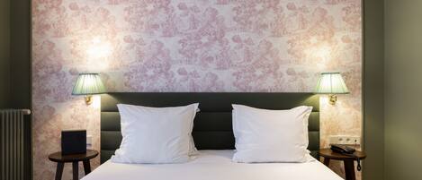 Una cama bien hecha con sábanas blancas, dos lámparas de noche y una pared con estampado floral.