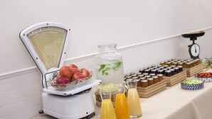 Una mesa de buffet con un bol de frutas, un exprimidor y diferentes condimentos.
