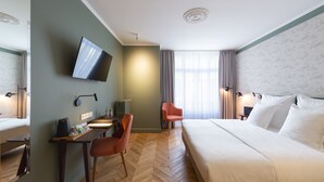 Una habitación de hotel con cama, escritorio con silla, televisor y ventana con cortinas.