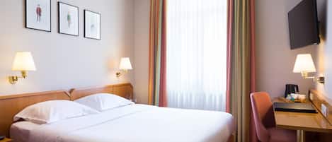 A hotel room with a large bed, two bedside tables with lamps, a desk with a chair, a flat-screen TV, and a window with curtains.