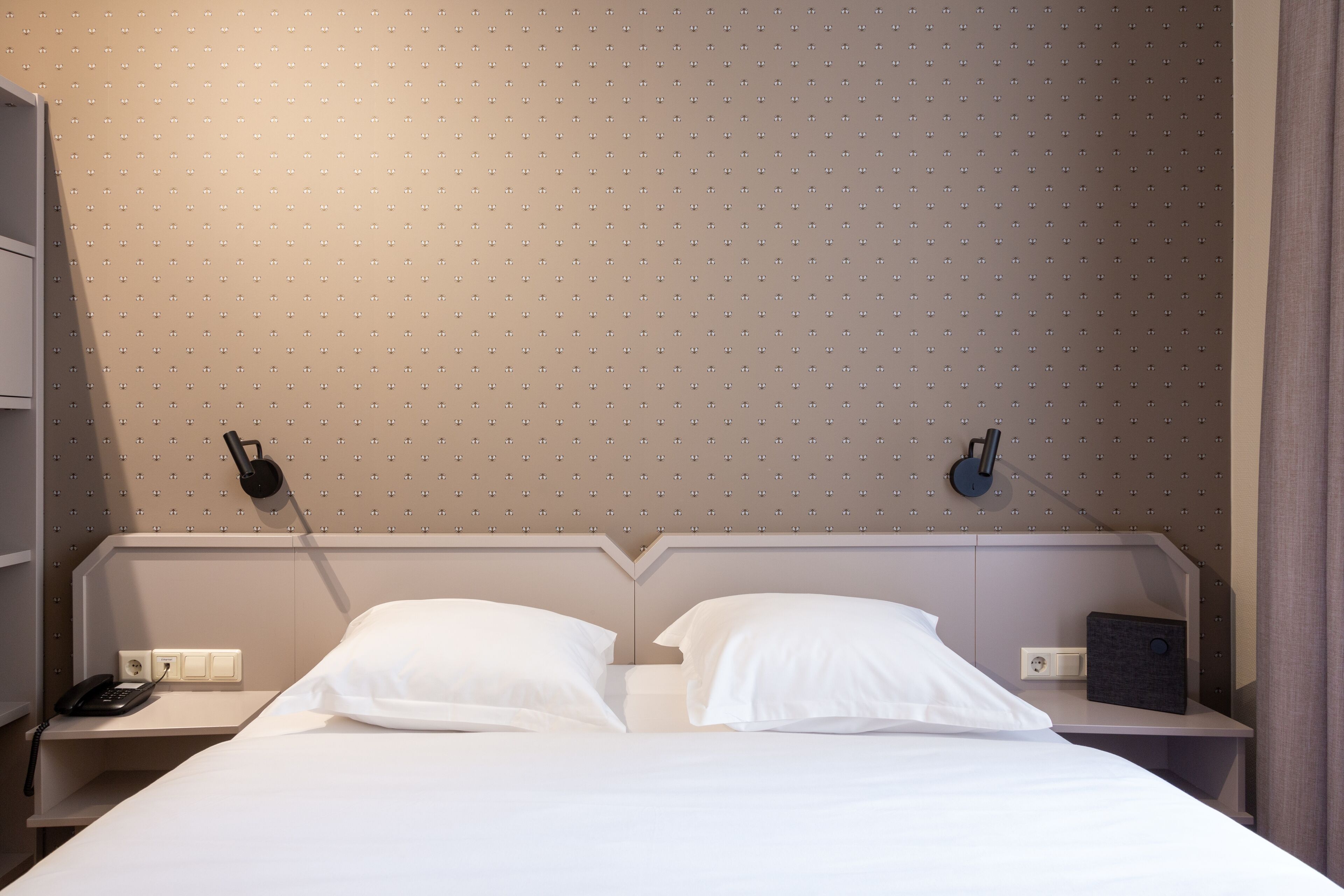 A hotel room with a bed, two bedside tables, a telephone, and a wall-mounted lamp.