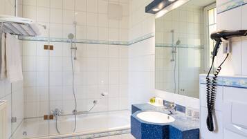 A bathroom with a glass-enclosed shower, a bathtub, a sink with a blue countertop, and a mirror with a telephone.