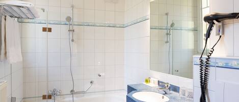 A bathroom with a glass-enclosed shower, a bathtub, a sink with a blue countertop, and a mirror with a telephone.