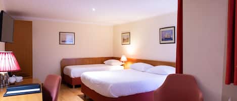 A hotel room with two beds, a desk with a lamp, a chair, and a small table with a magazine.