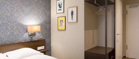Una habitación de hotel con cama, mesita de noche, lámpara de pared y armario con espejo.