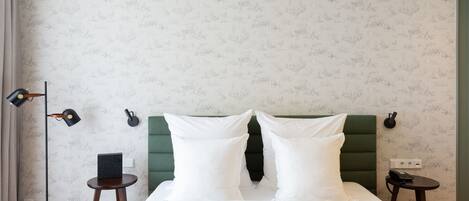 Una cama bien hecha con sábanas blancas, un cabecero tapizado en verde y dos mesitas de noche con lámparas.