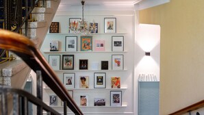 Una escalera con barandilla, un candelabro y una pared con cuadros enmarcados y alfombra estampada.