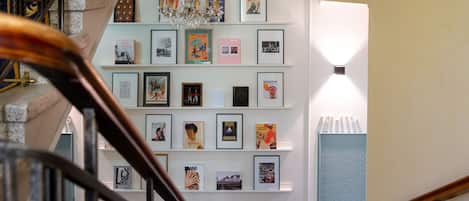 Una escalera con barandilla, un candelabro y una pared con cuadros enmarcados y alfombra estampada.