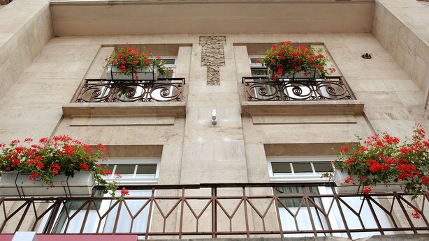 Fachada de un edificio con balcones, cada uno con una maceta llena de flores rojas.