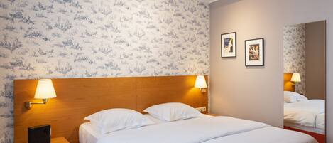 A hotel room with a wooden headboard, two bedside lamps, a bed with white linens, a nightstand with a lamp, and a mirror on the wall.