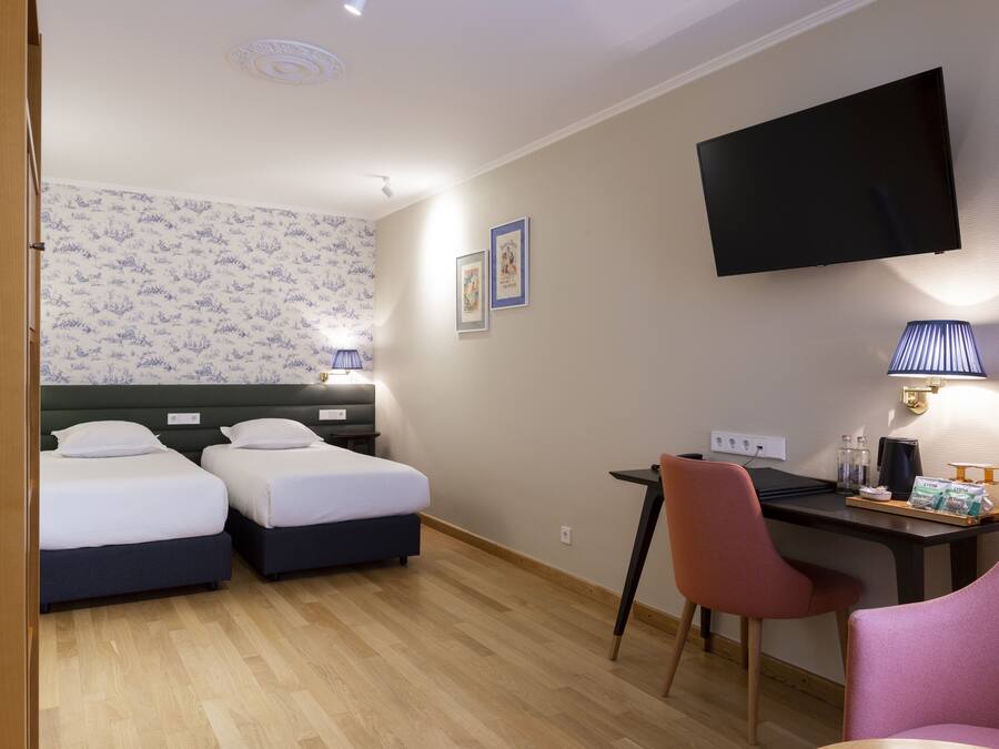 A hotel room with two beds, a desk, a chair, a TV, and a lamp.
