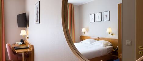 Una habitación de hotel con cama, lámparas de noche, escritorio con silla y televisor en la pared.