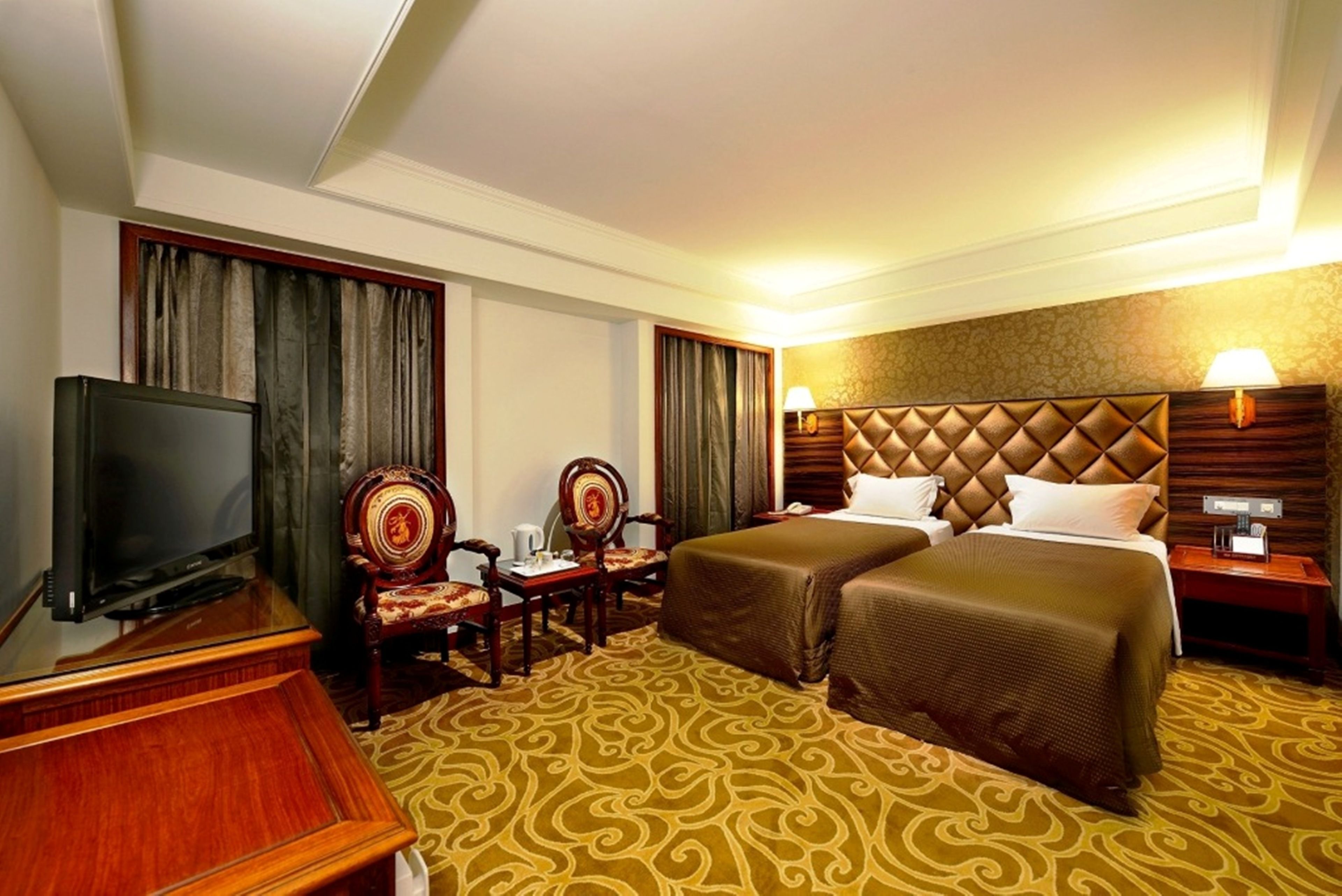A hotel room with two beds, a television, a desk with a chair, and a lamp.