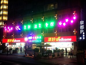 A building with multiple signs, including 'Top Good Welcome' and 'Top Good Welcome' in different languages. There are outdoor seating areas with umbrellas and potted plants. - Chyuan Du Spring Resort (Taipei)