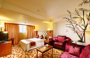 A hotel room with a bed, a TV, a desk, a chair, and a decorative plant. - Chyuan Du Spring Resort (Taipei)