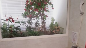Un baño con una bañera de mármol negro, una ventana con vistas a plantas, una toalla y un recipiente de madera.