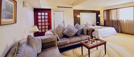 A hotel room with a large bed, a sofa, a coffee table, and a painting on the wall.