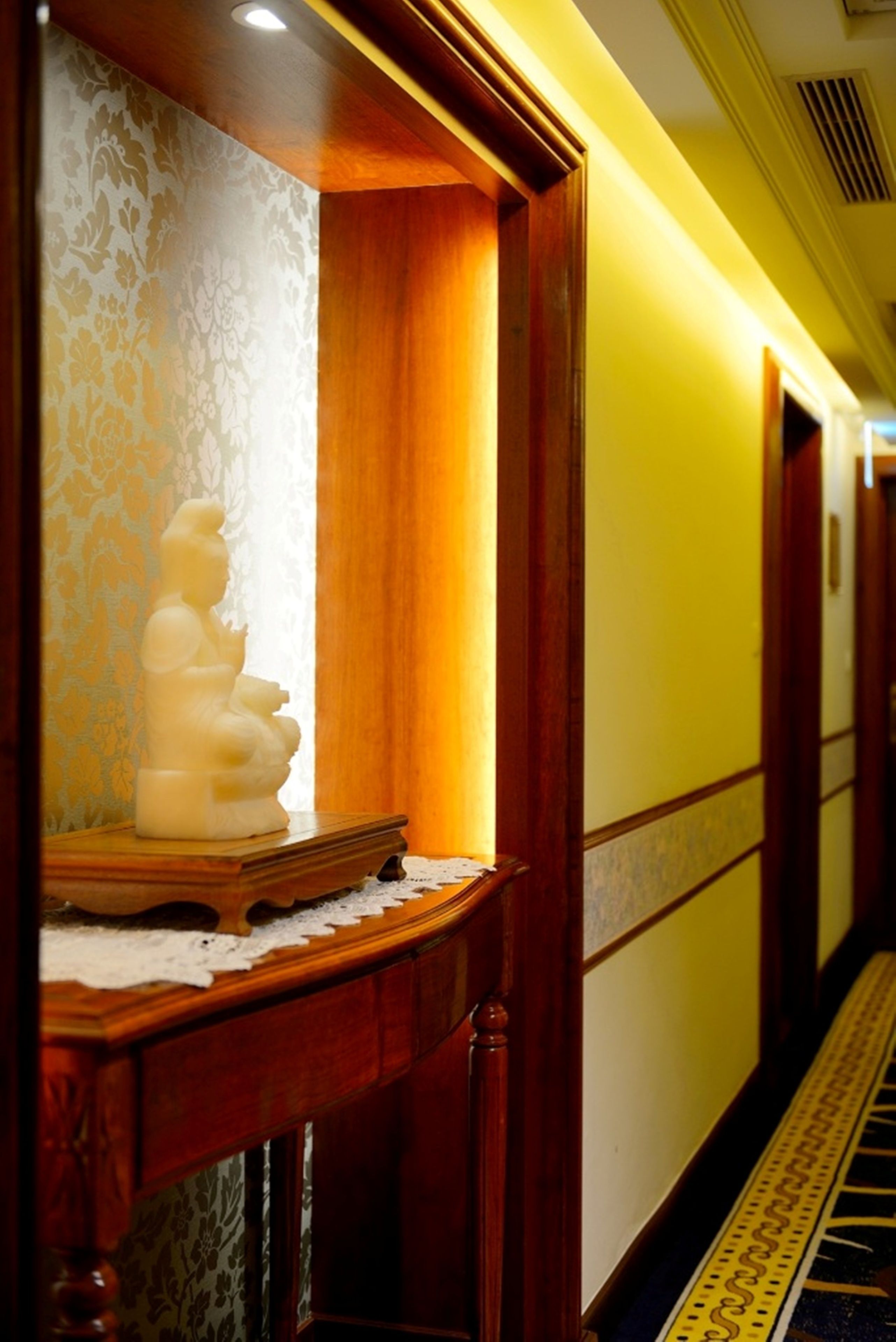 A hallway with a statue on a wooden table, patterned wallpaper, and a yellow wall.