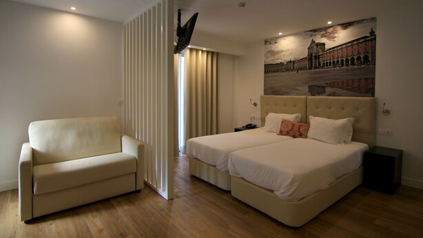 A hotel room with a sofa, two beds, a large mural, and a wooden floor.