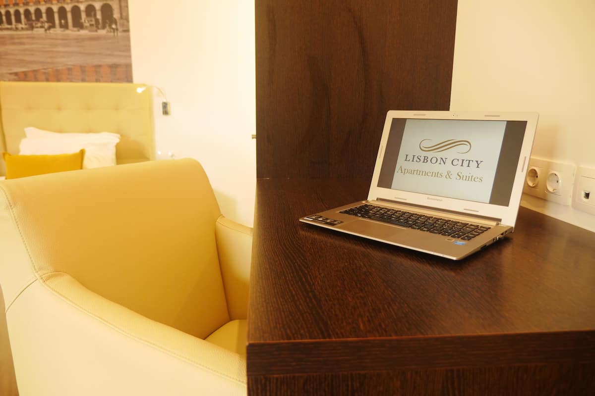 A laptop on a wooden desk with a screen displaying "Lisbon City Apartments & Suites".