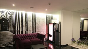 A lobby with a red sofa, a small table, a vending machine, and a decorative wall with vertical elements.