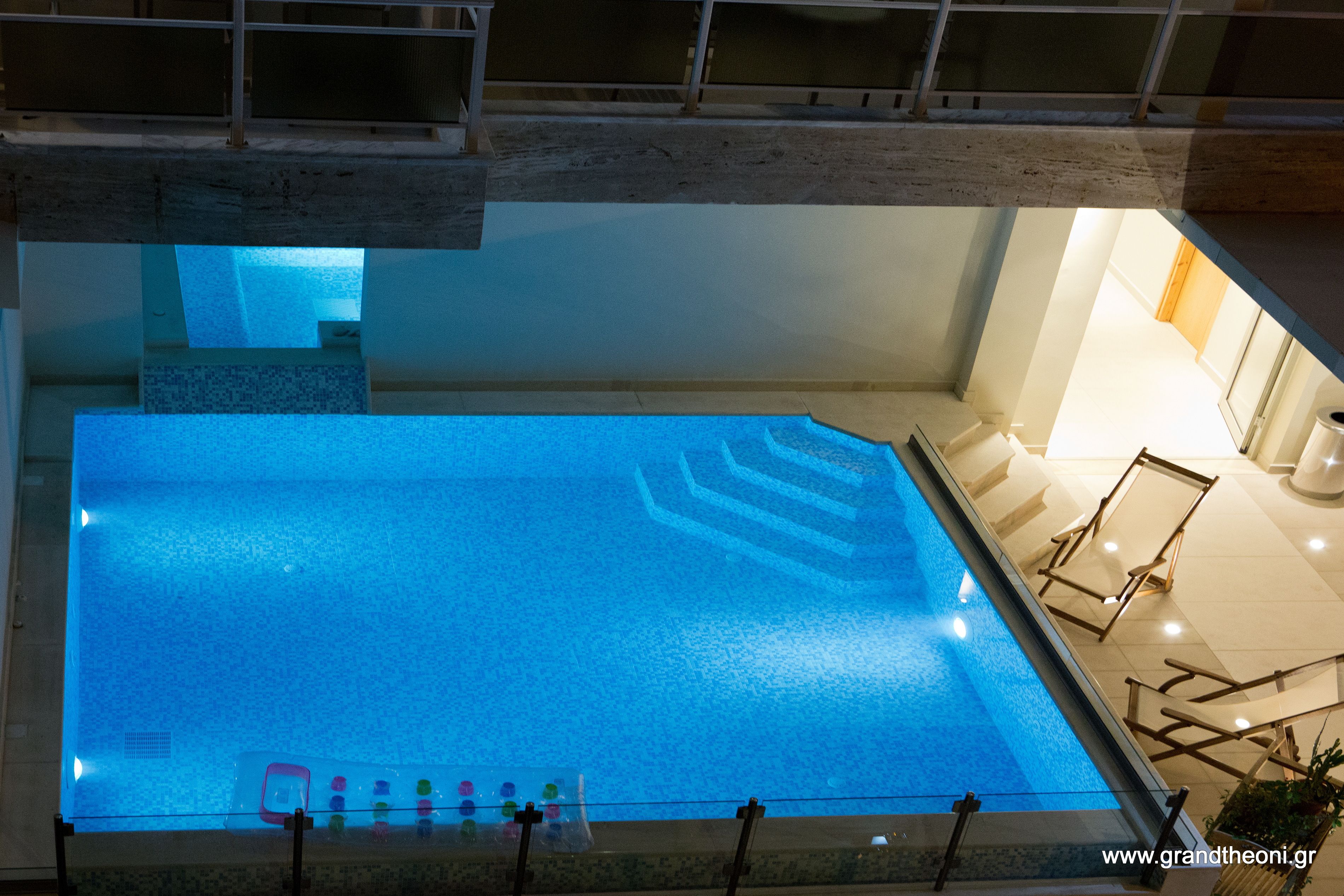 An indoor swimming pool with clear water, a glass barrier, and a staircase leading to an upper level.